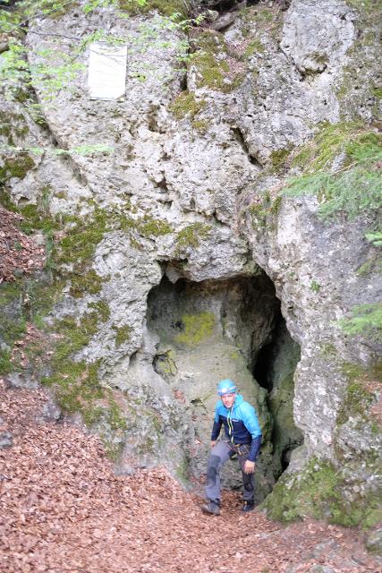 junger Mann mit Helm und Stirnlampe verlässt Höhle durch schmalen Ausgang