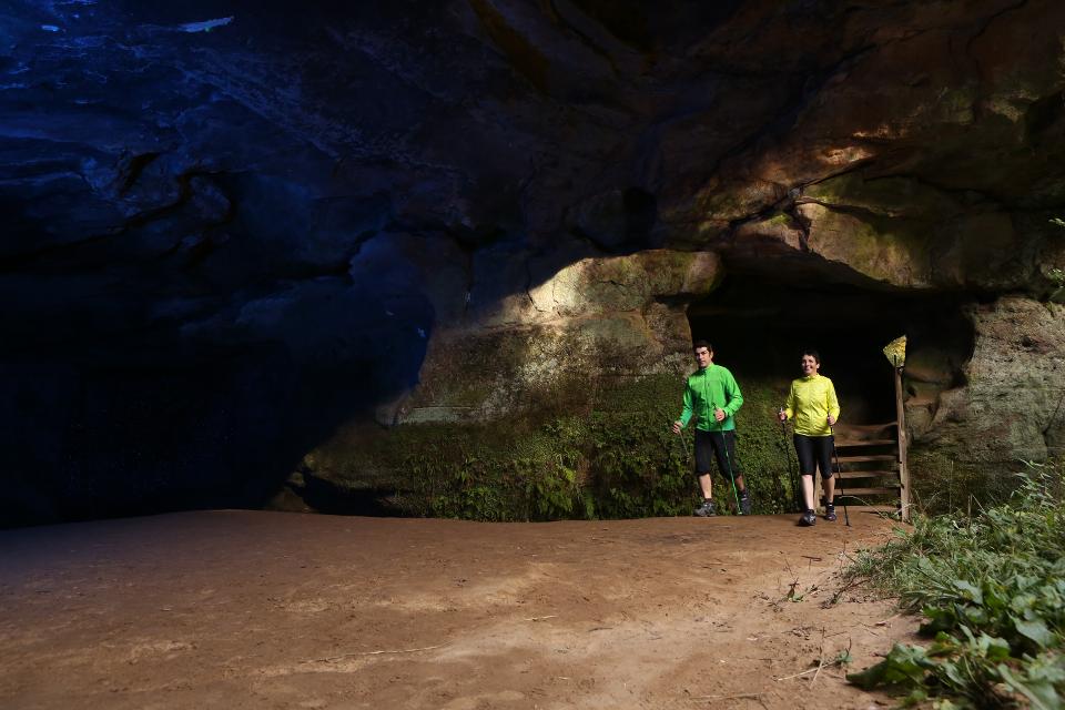 Paar geht mit Walkingstöcken durch die Karlshöhle, eine Sandsteinausspülung in der Schwarzachklamm, im Hintergrund Durchlass mit Stufen