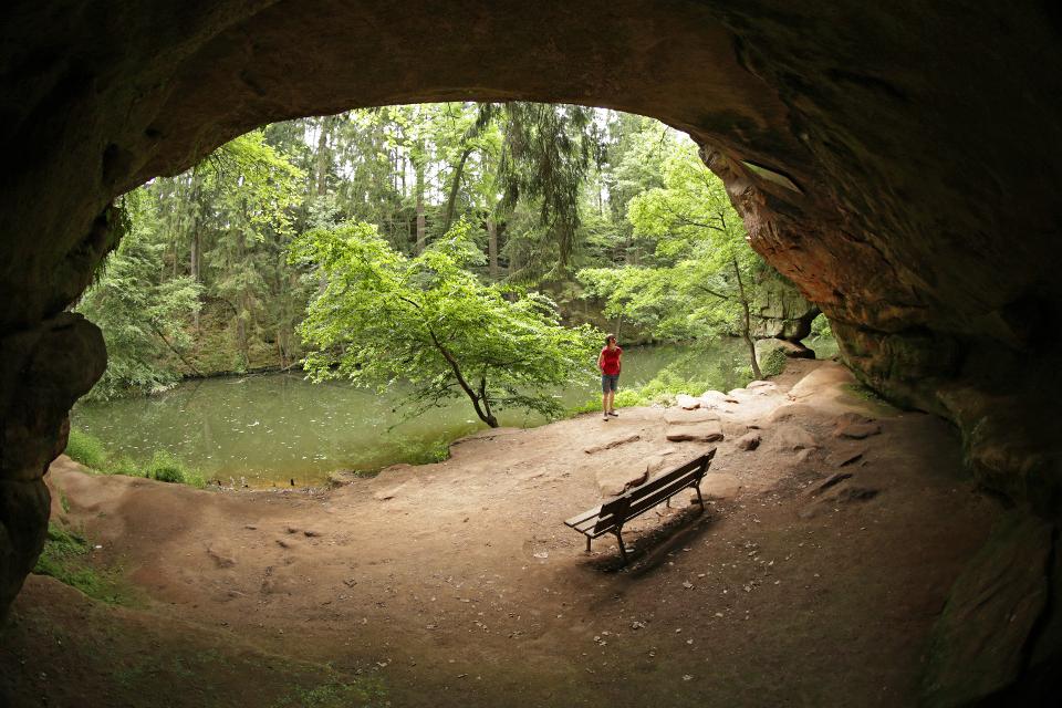 Blick aus der Höhle zur Schwarzach, im Vordergrund eine Sitzbank, am Ufer eine Person