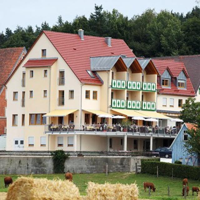 Landhotel mit umlaufender Terrasse, im Vordergrund Kühe auf der Weide