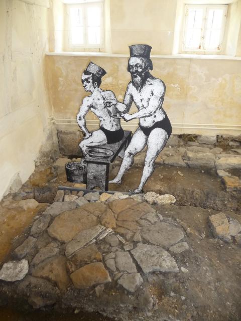Freigelegter alter Steinfußboden des mittelalterlichen Badhauses. Abbildungen vom Bader, der einen Kunden schröpft