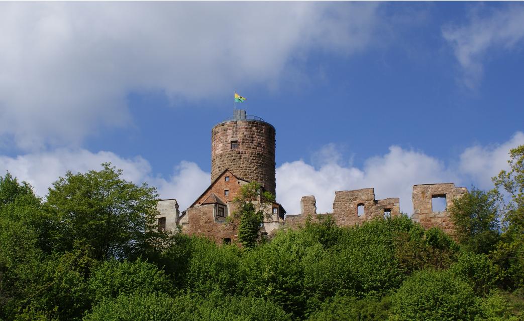 Ruinen der Burg und runder Burgturm vor blauem Himmel umringt von Büschen und Bäumen