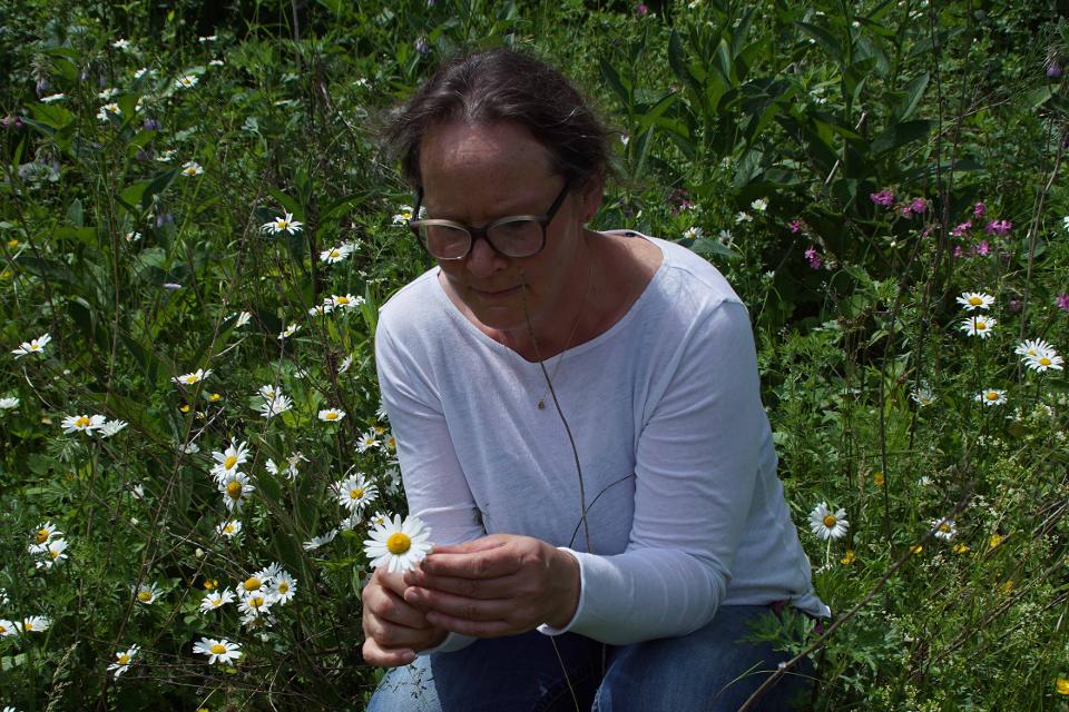 Melanie Grötsch kniet in Blumenwiese und hält eine Kamillenblüte in der Hand