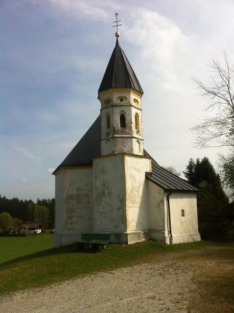 Eine in weiß gehaltene Kapelle steht an einem Waldrand