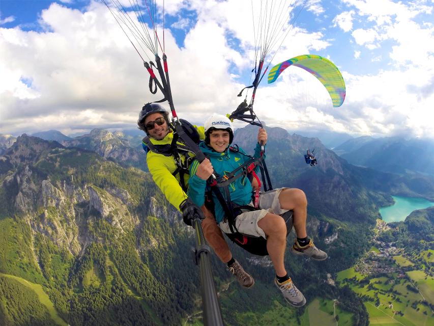 Der Betrachter blickt auf 2 Personen die mit einem Gleitschirm über die Alpen fliegen.