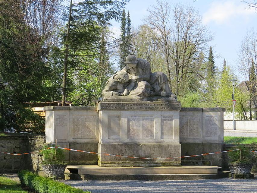 Der Betrachter blickt auf ein sehr großes Kriegerdenkmal aus Steinblöcken. Auf dem mittleren sind zwei verwundete Soldaten aus Stein dargestellt.