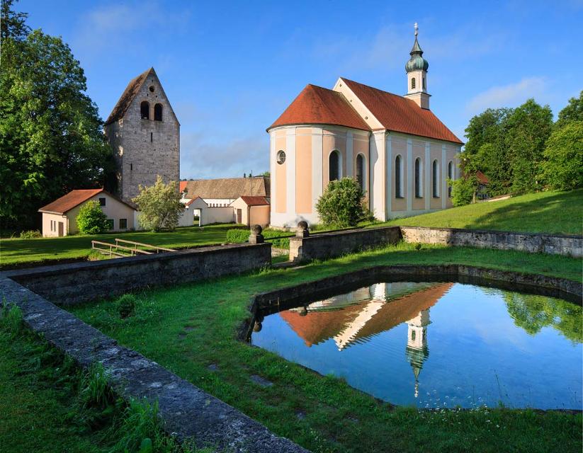 Der Betrachter blickt über einen Fischweiher hinüber zur barocken Kirche und dem romanischen Turm "Grauer Herzog".