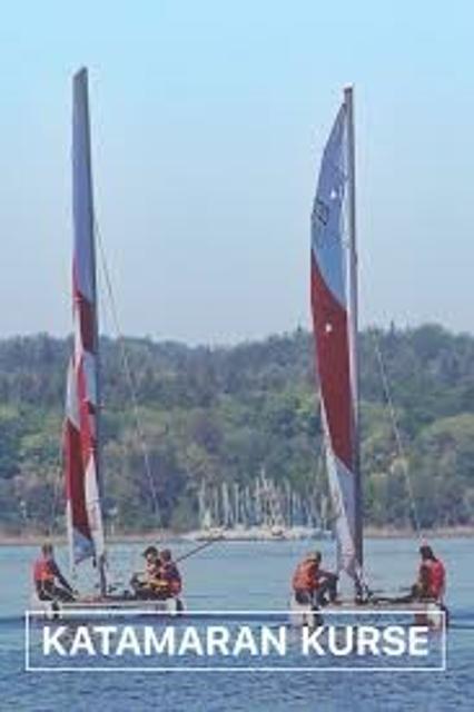 Der Betrachter blickt auf zwei Katamarane die über den See fahren, darunter mit dem Schriftzug "Katamaran Kurse"