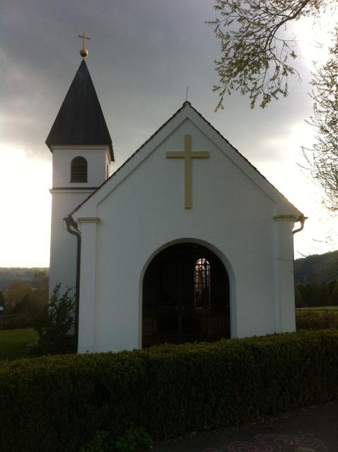 Der Betrachter blickt direkt auf eine schöne weiße Kapelle mit goldenem Kreuz über dem Eingangsportal.