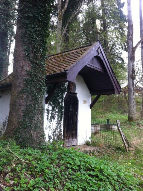 Der Betrachter sieht eine kleinere weiße Kapelle die im Wald steht.