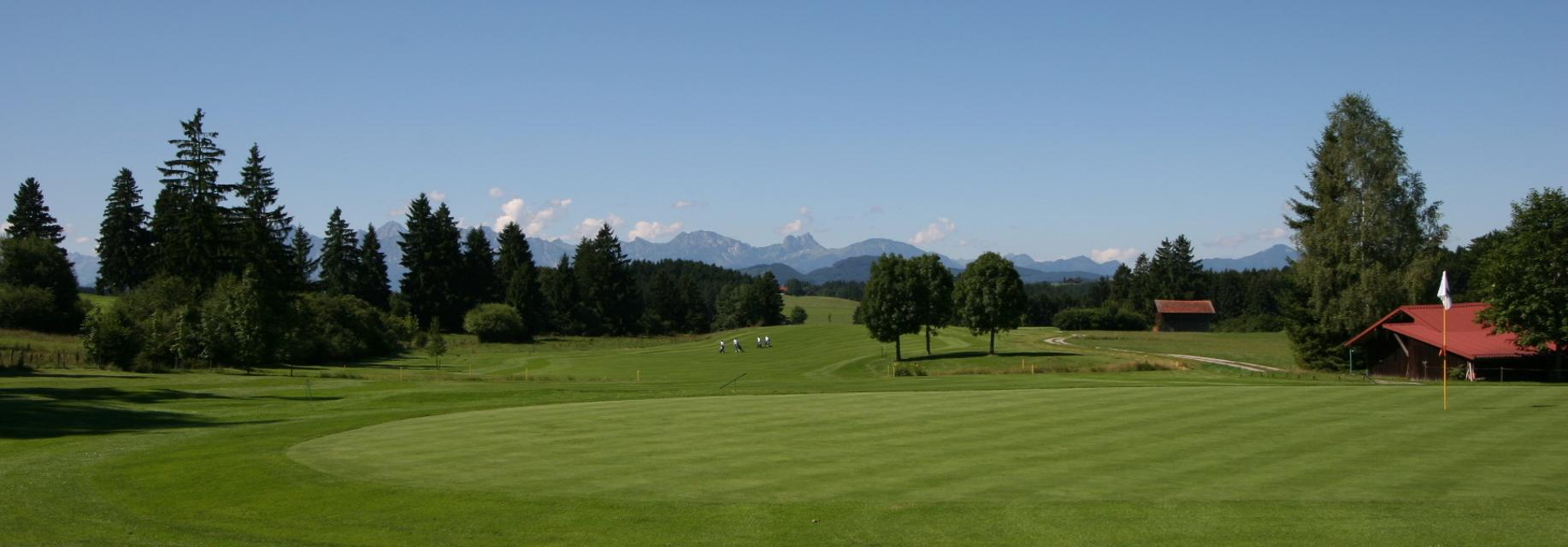 Der Betrachter blickt auf den Golfplatz und dem Alpenpanorama am Horizont.