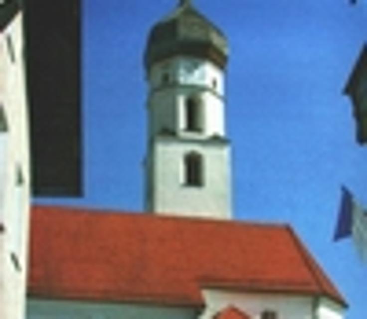 Durch zwei Häuser hindurch blickt der Betrachter auf das Dach und den Turm der barocken Pfarrkirche.