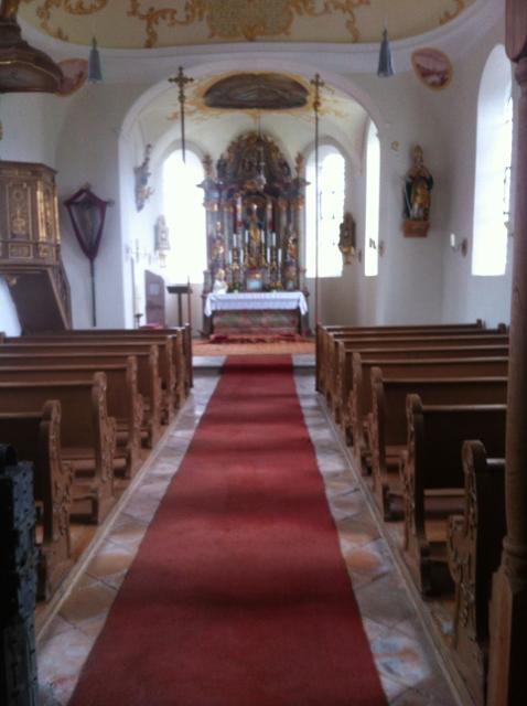 Der Blick führt den Mittelgang mit einem roten Teppich entlang nach vorne zum barock ausgestatteten Altarraum.