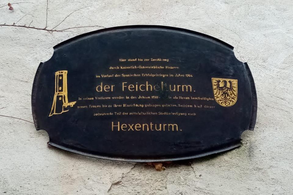 Der Betrachter blickt auf die Gedenktafel die an den ehemaligen Feichelturm an der Stadtmauer Schongau und den Insassen/Insassinen gedenken soll.