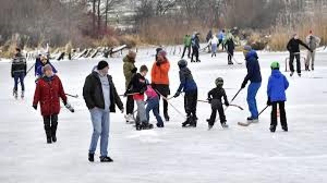 Auf einem großen zugefrorenen See tummeln sich viele Schlittschuhläufer und Eishockeyspieler.