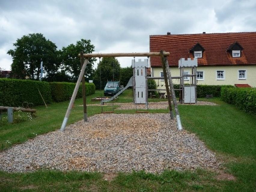 Der Spielplatz in Reichenau ist mit einer Spielburgkombination mit angebauter Reckstange, Doppelwippe, Rutsche, Schaukel, Federwippgerät und einem Sandkasten ausgestattet.