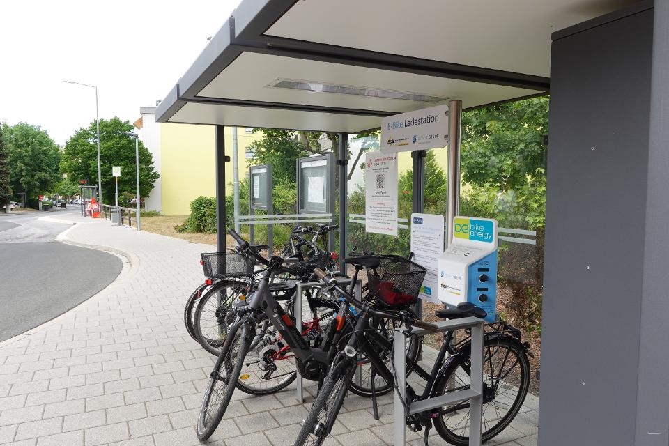 Ladestation mit Anschlüssen für 5 E-Bikes, 10 verschließbare Gepäckboxen und überdachte Fahrradparkplätze an der Endhaltestelle Goethering in der Schillerstraße.
                 title=
