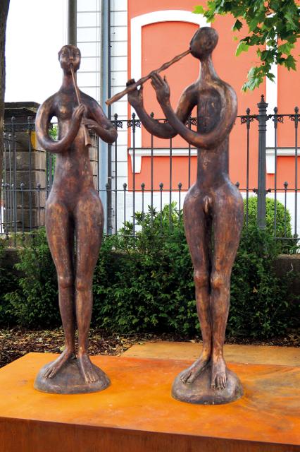 2016 wurde der kleine Platz neben der Sparkasse offiziell benannt und dabei das Skulpturenpaar enthüllt. Die schlanken, in ihrer Körperlichkeit ausgeprägten Flötenspieler deuten auf Jugendlichkeit im Gleichklang einer Melodie hin. Mann und Frau stehen zugewandt beieinander, und doch ist jeder ...