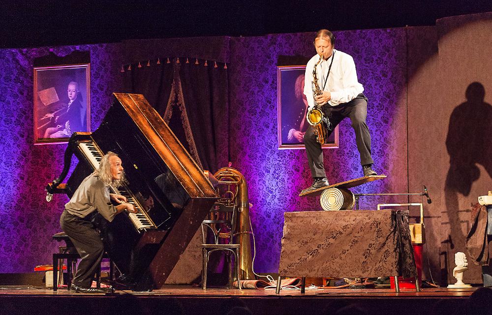 Die Künstler Gogol und Mäx spielen Klavier und Saxophon, während sie akrobatische Kunststücke aufführen.