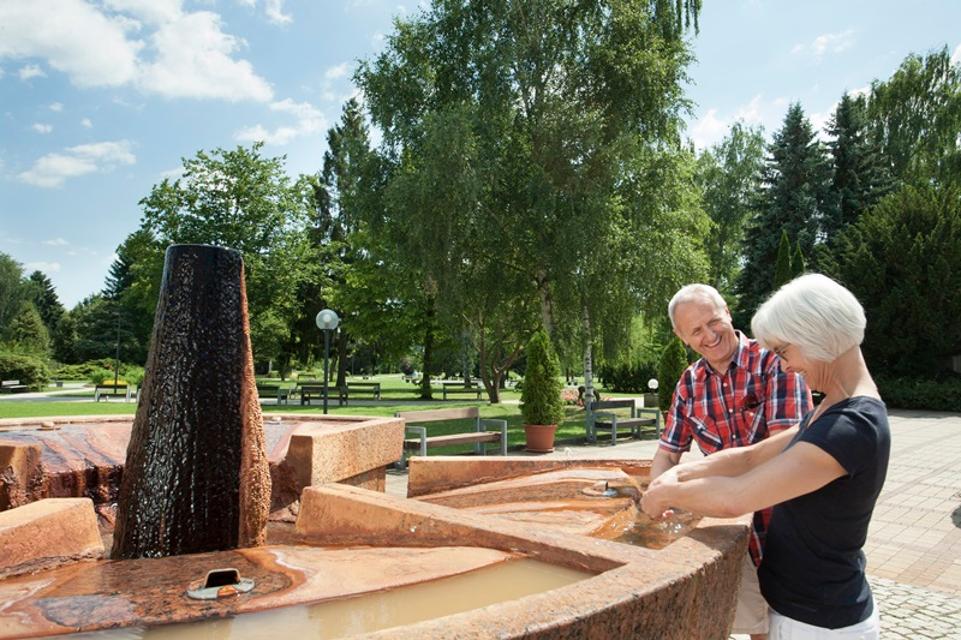 Ein Paar badet seine Arme in der Natur-Sole des König-Heinrich-Brunnens im Kurpark Bad Soden-Salmünster title=