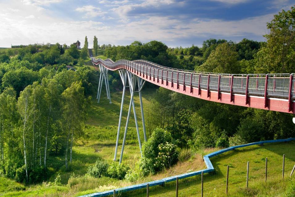 Seit dem Jahr 2007 ist die Drachenschwanzbrücke in der NEUEN LANDASCHAFT Ronneburg ein Besuchermagnet.
Mit ihren 225 Metern und der einzigartigen Form ist sie eine der längsten innovativsten Holzbrücken in Deutschland. Technische Innovationen birg...
